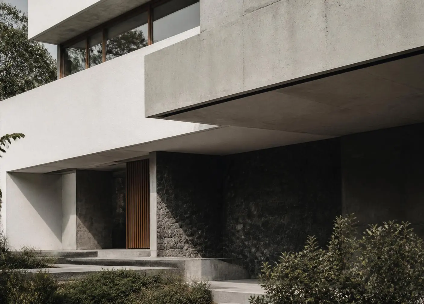 Vivienda contemporánea con grandes ventanas, voladizo de hormigón y base de piedra volcánica